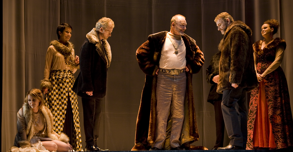 The cast of King Lear standing on stage looking at the king, who is standing in the middle