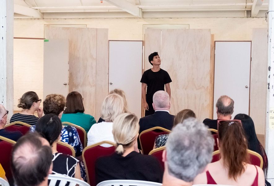 Teenage boy performs a monologue in front of a seated crowd