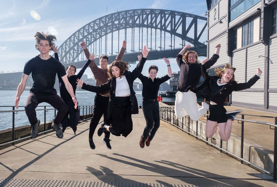 Group of young people jumping off the ground in front of the Sydney Harbour Bridge